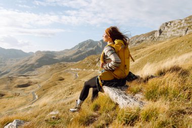 Dağ yamacında gezen genç bir bayan gezgin manzaranın tadını çıkarıyor. Macera aktif. Dağ tırmanışı.