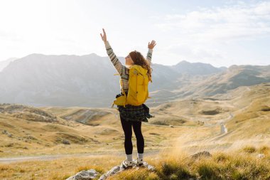 Dağ yamacında gezen genç bir bayan gezgin manzaranın tadını çıkarıyor. Macera aktif. Dağ tırmanışı.