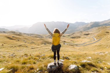 Dağ yamacında gezen genç bir bayan gezgin manzaranın tadını çıkarıyor. Macera aktif. Dağ tırmanışı.