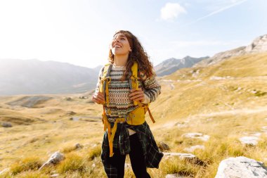 Dağ yamacında gezen genç bir bayan gezgin manzaranın tadını çıkarıyor. Macera aktif. Dağ tırmanışı.