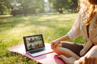Çevrimiçi eğitim, rota. Parkta dizüstü bilgisayarın önünde yoga yapan bir kadın. Sağlıklı yaşam tarzı, spor.