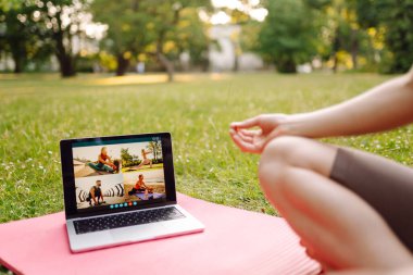 Çevrimiçi eğitim, rota. Parkta dizüstü bilgisayarın önünde yoga yapan bir kadın. Sağlıklı yaşam tarzı, spor.