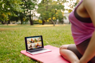Çevrimiçi eğitim, rota. Parkta dizüstü bilgisayarın önünde yoga yapan bir kadın. Sağlıklı yaşam tarzı, spor.