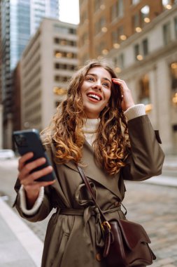 Şık bir kadın sokakta dururken akıllı telefonuyla internette geziniyor. Sonbahar havası. Yaşam tarzı, seyahat, iletişim, teknoloji.