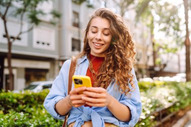 Şehirde telefonla dolaşan genç bir kadın. Çevrimiçi arkadaşlarla sohbet. Teknoloji, blog yazma. Moda tarzı.