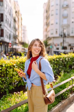 Şehirde telefonla dolaşan genç bir kadın. Çevrimiçi arkadaşlarla sohbet. Teknoloji, blog yazma. Moda tarzı.