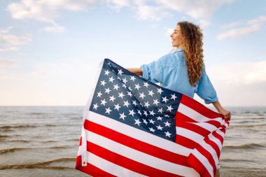 Okyanusta yürüyen Amerikan bayrağı taşıyan genç bir kadın. Amerika Bağımsızlık Günü konsepti. 4 Temmuz.