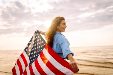Okyanusta yürüyen Amerikan bayrağı taşıyan genç bir kadın. Amerika Bağımsızlık Günü konsepti. 4 Temmuz.