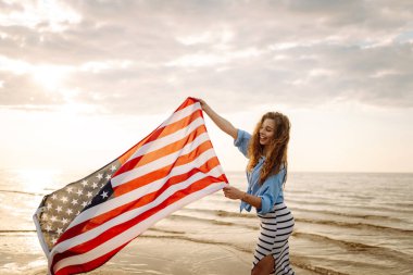 Okyanusta yürüyen Amerikan bayrağı taşıyan genç bir kadın. Amerika Bağımsızlık Günü konsepti. 4 Temmuz.