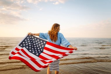 Okyanusta yürüyen Amerikan bayrağı taşıyan genç bir kadın. Amerika Bağımsızlık Günü konsepti. 4 Temmuz.