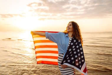 Okyanusta yürüyen Amerikan bayrağı taşıyan genç bir kadın. Amerika Bağımsızlık Günü konsepti. 4 Temmuz.