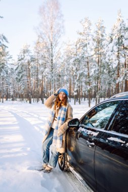 Güzel genç bir kadın kış zamanı dışarıda otomobilinin yanında. Araba yolculuğu, tatil kavramı. Kış tatili.