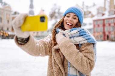 Kış kıyafetleri içinde gülümseyen kadın akıllı telefondan selfie çekiyor. Selfie zamanı. Tatiller, dinlenme, blog yazma