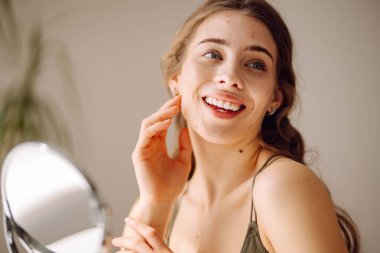 Güzel bir kadın aynaya bakıyor, eliyle yüzüne dokunuyor. Sivilceler, sivilceler, gözenekler, yaralar. Filtresiz doğal cilt