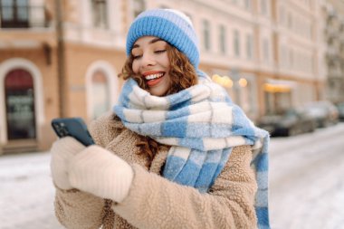 Caddede yürüyen çekici bir kadın ve karlı şehir merkezinde akıllı telefondan mesaj atıyor. Çevrimiçi iletişim. Teknoloji konsepti.
