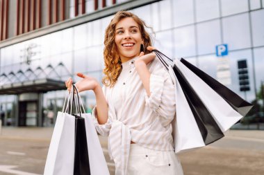 Alışveriş torbalı şık bir kadın şehrin sokaklarında yürüyor. Kara Cuma. Satış, moda, alışverişler.