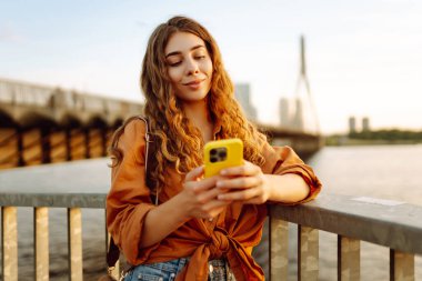Dışarıda telefon kullanan bir kadın. Sonbahar kıyafetleri içinde, setin üzerinde telefonu olan genç bir kadın. Arkadaşlarla Çevrimiçi İletişim.