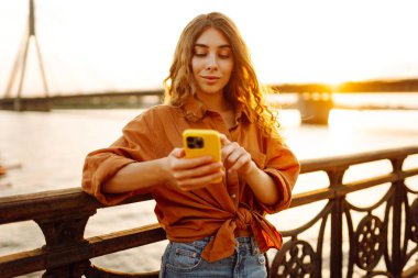 Dışarıda telefon kullanan bir kadın. Sonbahar kıyafetleri içinde, setin üzerinde telefonu olan genç bir kadın. Arkadaşlarla Çevrimiçi İletişim.