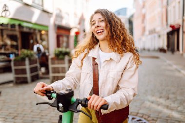 Mutlu kadın güneşli bir günde şehir caddesinde elektrikli scooter kullanıyor. Ekolojik nakliye. Etkin yaşam biçimi.