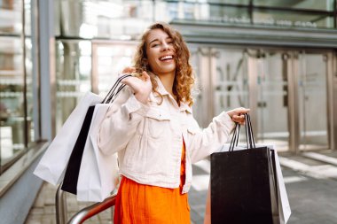 Alışveriş yaptıktan sonra alışveriş torbalarıyla şehirde dolaşan mutlu bir kadın. Tüketim, satış, alım, alışveriş, yaşam tarzı konsepti.