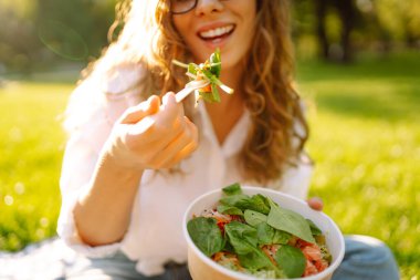 Mutlu kadın güneşli bir parkta piknikte otururken sağlıklı yeşil sebze salatası yiyor. Vejetaryen.