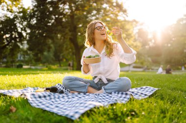 Mutlu kadın güneşli bir parkta piknikte otururken sağlıklı yeşil sebze salatası yiyor. Vejetaryen.