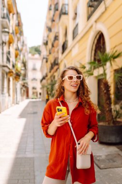 Şehir caddesinde telefonla yürüyen güzel bir kadın. Yaşam tarzı, seyahat, turizm, teknoloji, blog yazma, iletişim kavramı.