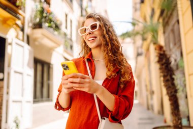 Şehir caddesinde telefonla yürüyen güzel bir kadın. Yaşam tarzı, seyahat, turizm, teknoloji, blog yazma, iletişim kavramı.