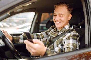 Arabada sürücü koltuğunda oturan akıllı telefonu kullanan gülümseyen adam. Araba yolculuğu, yaşam tarzı konsepti..