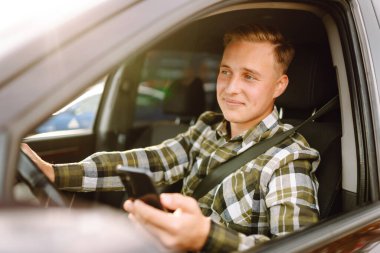 Arabada sürücü koltuğunda oturan akıllı telefonu kullanan gülümseyen adam. Araba yolculuğu, yaşam tarzı konsepti..