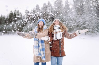 Moda kıyafetleri ve atkıları olan iki genç bayan. Kış parkında sokakta poz veren kaygısız kadınlar. Kış anlarının tadını çıkarıyorum.