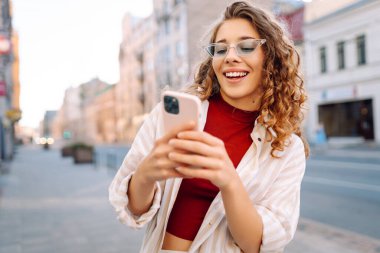 Gün batımında dışarıda dikilirken akıllı telefon kullanan bir kadın. Teknoloji, bağlantı, blog yazma, modern yaşam tarzı kavramı