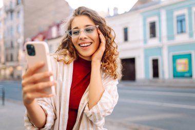 Gün batımında dışarıda dikilirken akıllı telefon kullanan bir kadın. Teknoloji, bağlantı, blog yazma, modern yaşam tarzı kavramı