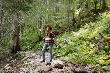 Sırt çantalı bir kadın sık ormanda yer yolunda yürüyor. Temiz hava ve vahşi doğa. Yürüyüş.