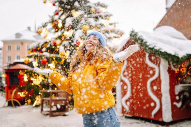 Genç bir kadın kışın Noel pazarında güler ve kar fırlatır. Işıklar yansın. Kış tatili.