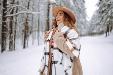 Gülümseyen genç kadın karlı kış parkında kış havasının tadını çıkarıyor. Boho tarzı. Tatiller, dinlenme, seyahat konsepti.