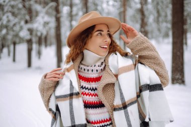 Gülümseyen genç kadın karlı kış parkında kış havasının tadını çıkarıyor. Boho tarzı. Tatiller, dinlenme, seyahat konsepti.