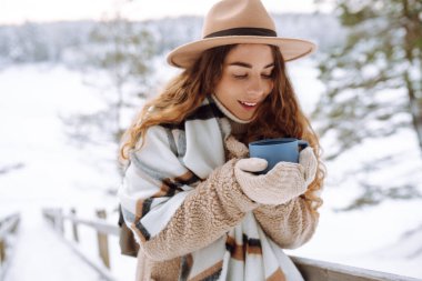Karlı bir ormanda termosla doğanın tadını çıkaran genç bir kadın. Kış yürüyüşü. Seyahat, turizm, doğa, aktif yaşam tarzı.