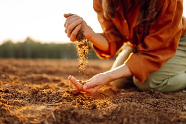 Kadınların elleri tarladaki kara toprakları ayırıyor. Kırsalda güneşli bir öğleden sonra toprağı elleriyle inceleyen genç bir çiftçi kadın. Verimli topraklar.