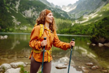 Sarı sırt çantalı genç turist kadın bir dağ gölünün arka planında duruyor. Seyahat, macera. Etkin bir yaşam biçimi kavramı.