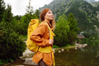 Sarı sırt çantalı genç turist kadın bir dağ gölünün arka planında duruyor. Seyahat, macera. Etkin bir yaşam biçimi kavramı.