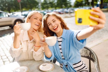 Selfie zamanı! Açık kahve dükkanında otururken akıllı telefon selfie 'si kullanan hoş bayan arkadaşlar. Moda, güzellik, blog yaşam tarzı.