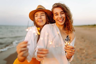 Güzel iki kadın sahilde maytap kutlaması yapıyor. Birlikte harika vakit geçiriyorlar! Yaz tatili, parti, tatil, dinlenme.