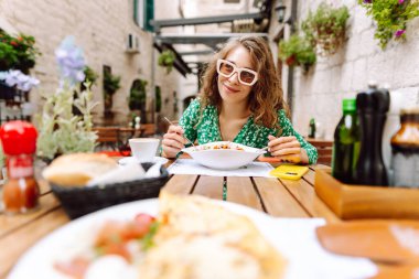 İtalyan makarnası yiyen ve Roma caddesindeki restoranda kahve içen bir kadın. İtalyan gastronomisi ve seyahati kavramı.