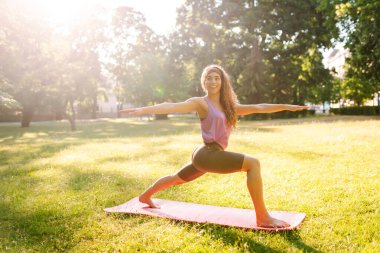 Eşofmanlı genç bayan antrenör halk parkında yoga pozunu değiştiriyor. Yaşam tarzı ve meditasyon konsepti.