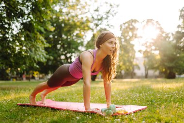 Eşofmanlı genç bayan antrenör halk parkında yoga pozunu değiştiriyor. Yaşam tarzı ve meditasyon konsepti.