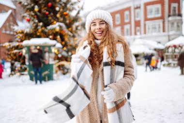 Mutlu bir turist kadın, kış boyunca kar ve aydınlatılmış süslemelerle bir Noel pazarında duruyor. Yeni yıl. Kış tatili.