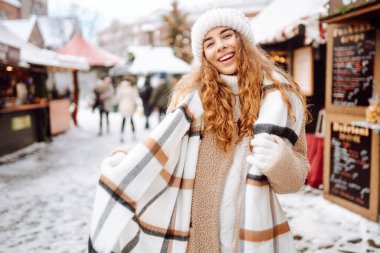 Mutlu bir turist kadın, kış boyunca kar ve aydınlatılmış süslemelerle bir Noel pazarında duruyor. Yeni yıl. Kış tatili.