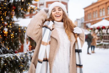 Mutlu bir turist kadın, kış boyunca kar ve aydınlatılmış süslemelerle bir Noel pazarında duruyor. Yeni yıl. Kış tatili.