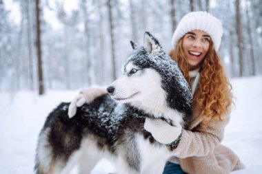 Güzel genç bir kadın köpeğiyle kış ormanında yürüyor. Sümüklü köpek. Evcil hayvan sahibi köpeğini dışarıda gezdirmekten hoşlanır. Dostluk konsepti, evcil hayvanlar.